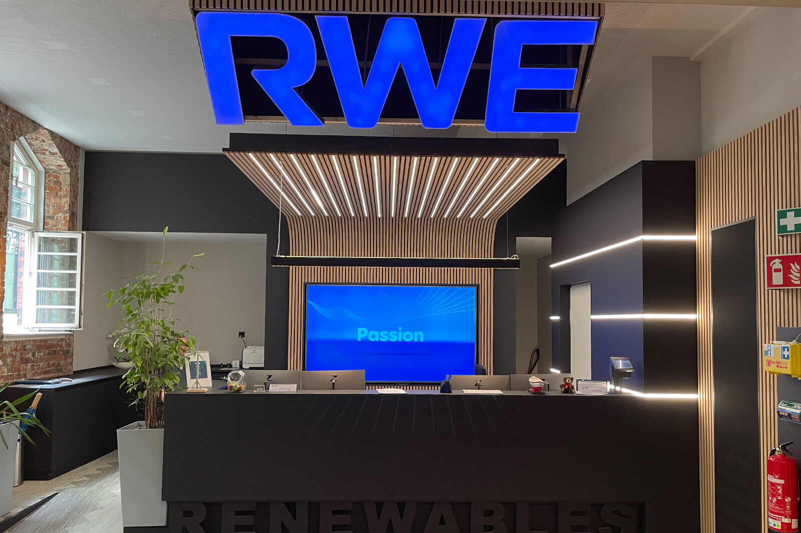 Der Empfangsbereich von RWE mit einem blauen Logo, einem Bildschirm mit dem Wort 'Passion' und modernen Holzelementen.