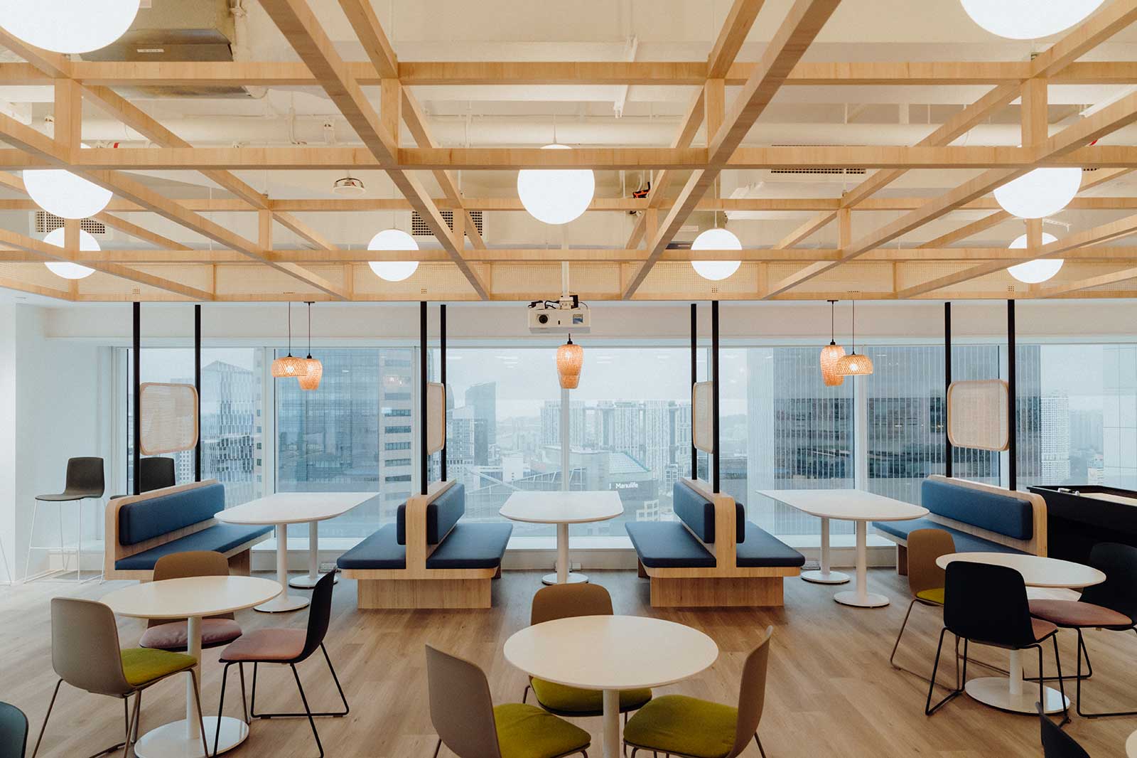 Helle Cafeteria mit großen Fenstern, Holzmöbeln, Sitzbänken und einem modernen Beleuchtungssystem.