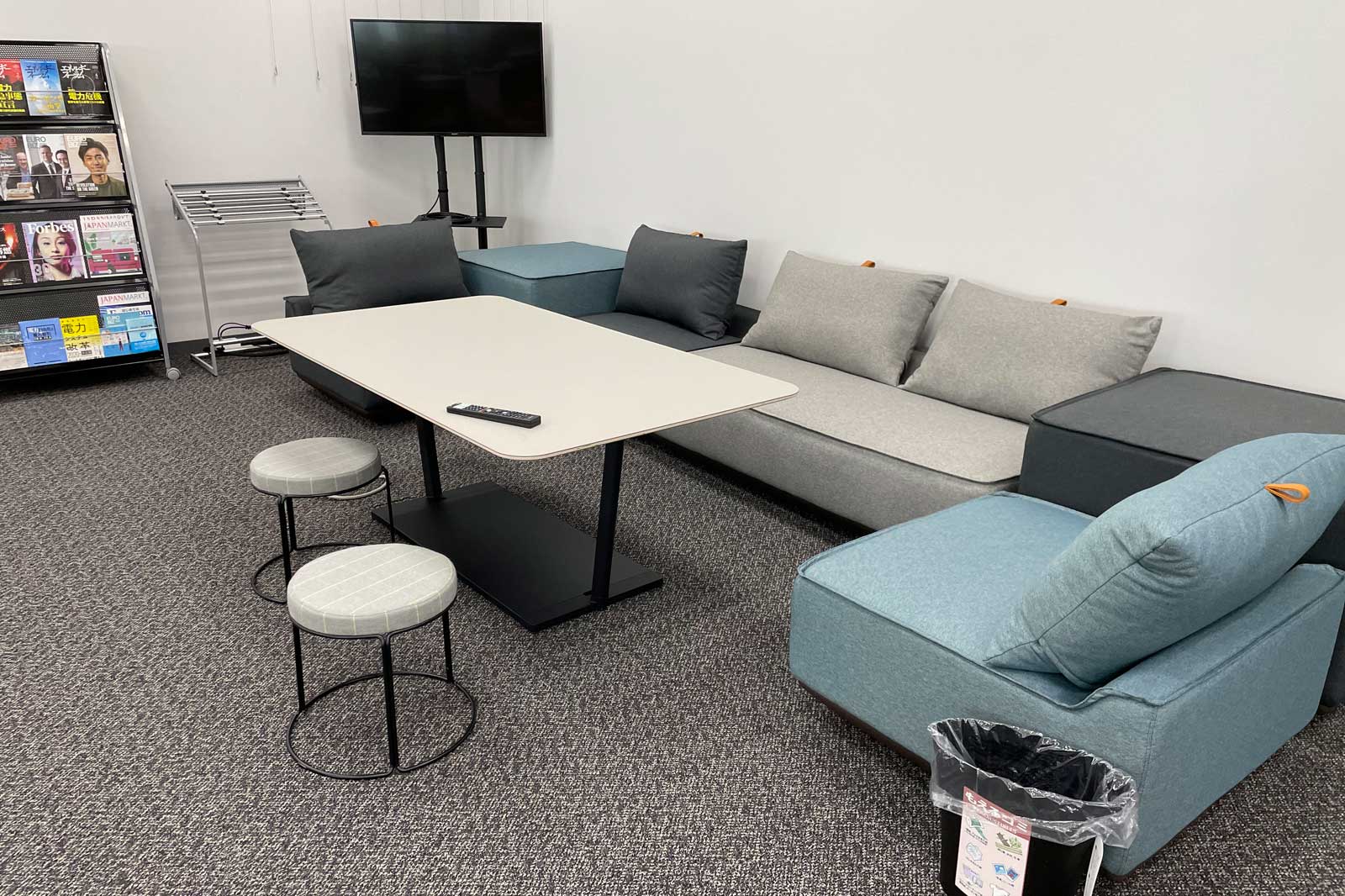 Ein moderner Aufenthaltsraum mit einem Tisch, bequemen Sofas, Hockern und einem Fernseher an der Wand.