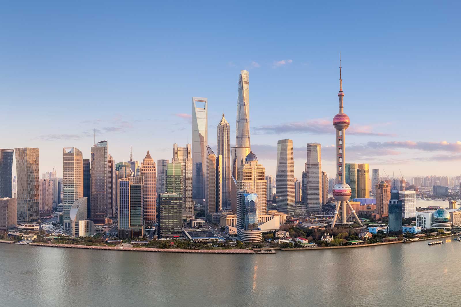 A panoramic view of Shanghai's skyline featuring skyscrapers, the Oriental Pearl Tower, and the Huangpu River at sunset.