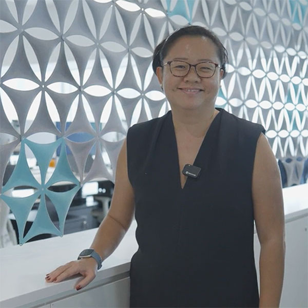 A person in a dark sleeveless dress standing beside a patterned wall with a modern design.
