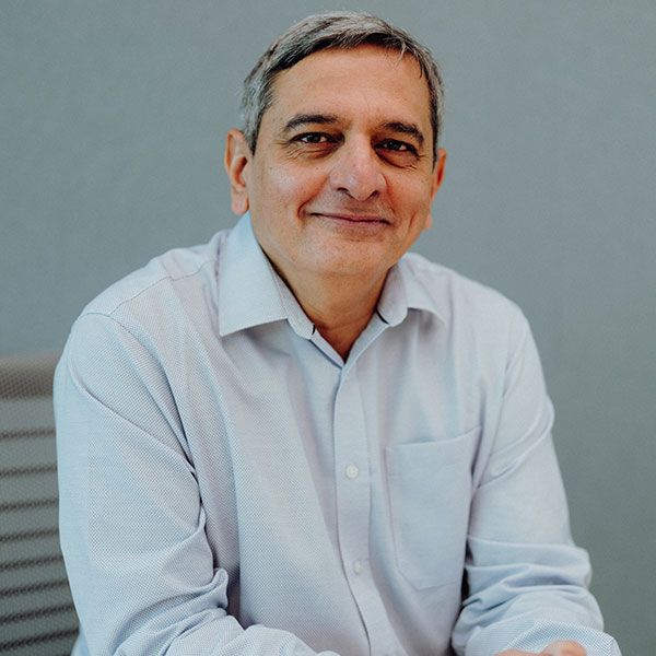 A person wearing a light blue shirt, seated in front of a grey background.