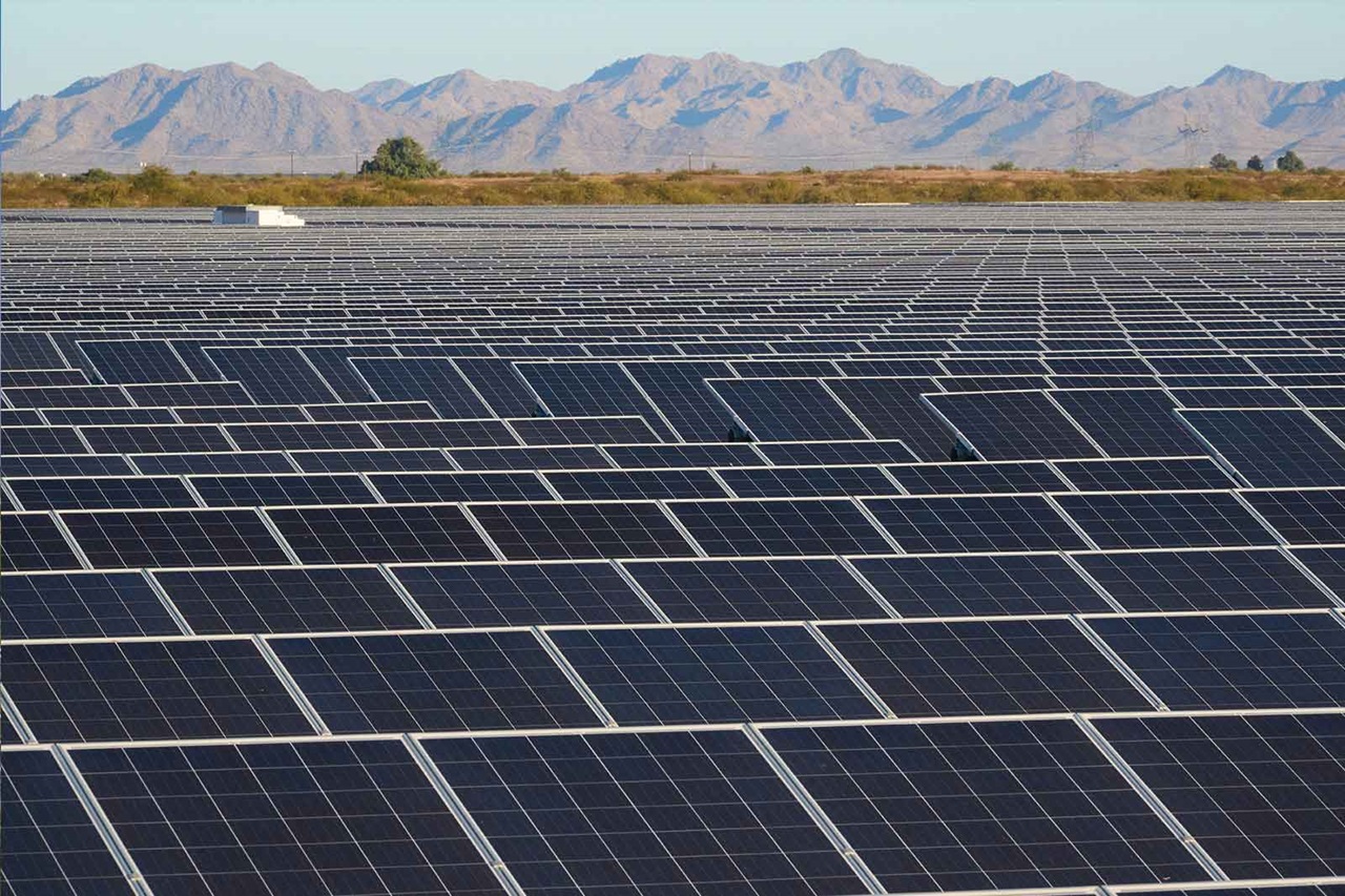 Ein weitläufiges Solarpanel-Feld mit vielen schwarzen Solarpanels vor einem Hintergrund aus Bergen.