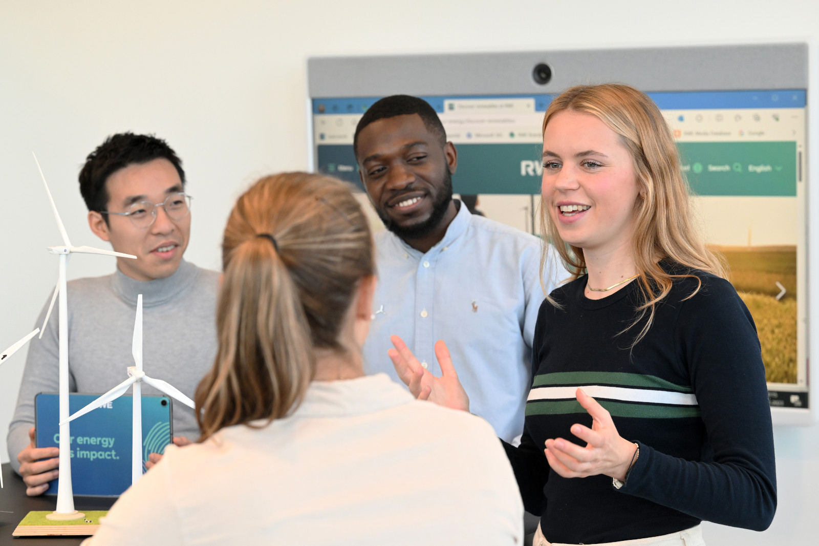 Eine Gruppendiskussion über erneuerbare Energie mit einem Windkraftmodell im Vordergrund.