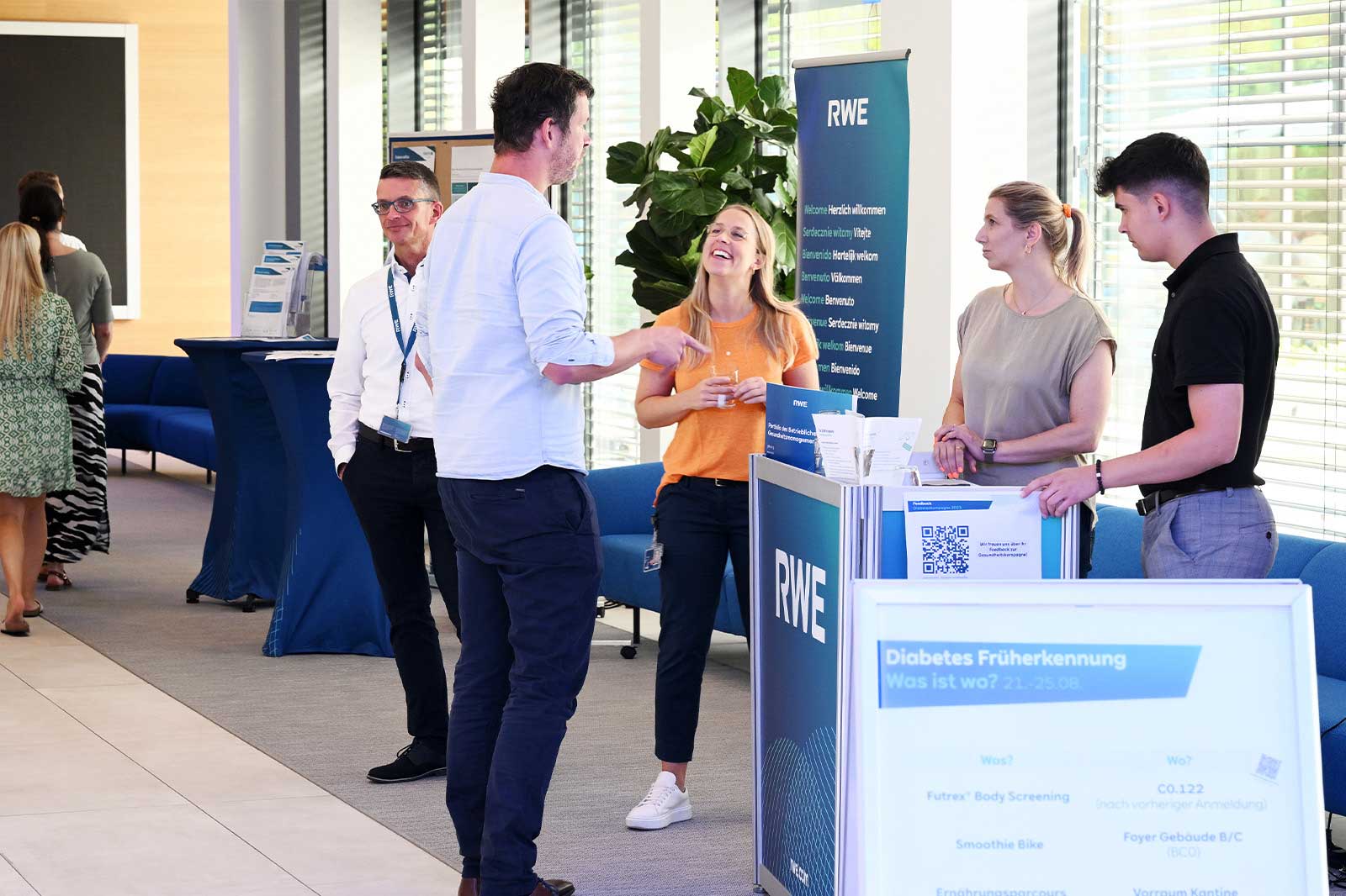 Eine professionelle Veranstaltung bei RWE mit Teilnehmern an einem Informationsstand, die über Diabetes-Screening-Dienste sprechen.