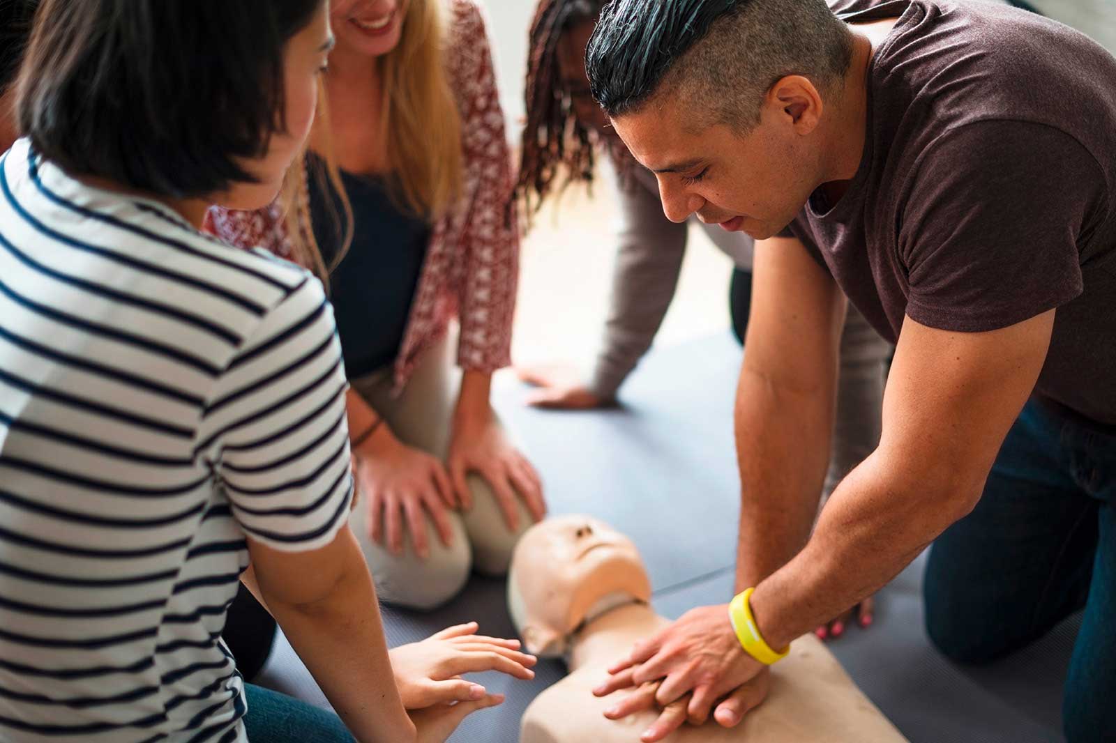 Eine Gruppe von Menschen übt die Herz-Lungen-Wiederbelebung an einer Trainingspuppe in einem hellen Raum und konzentriert sich auf die richtige Technik.