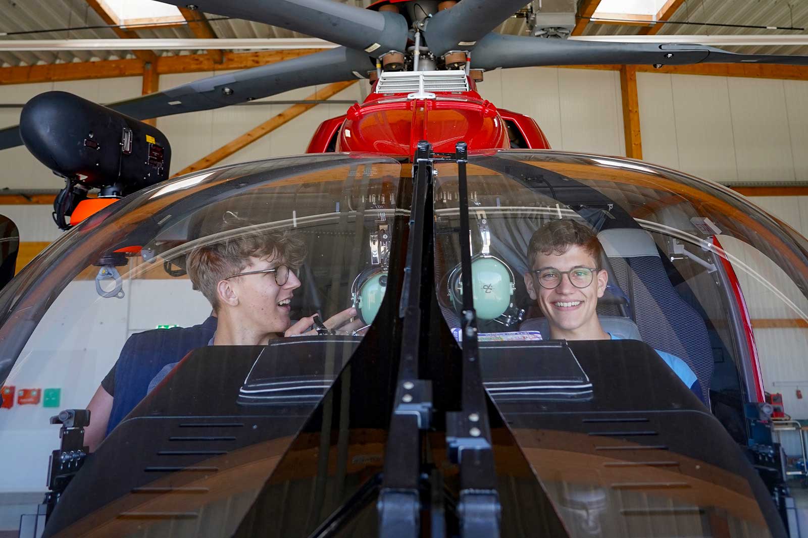 Zwei Personen sitzen im Cockpit eines roten Hubschraubers und konzentrieren sich auf die Instrumententafeln und Anzeigen.