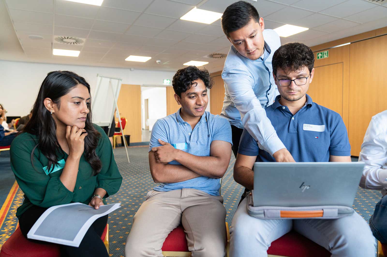 Eine Gruppe von Personen diskutiert konzentriert, mit einem Laptop auf dem Tisch in einem gut beleuchteten Raum.