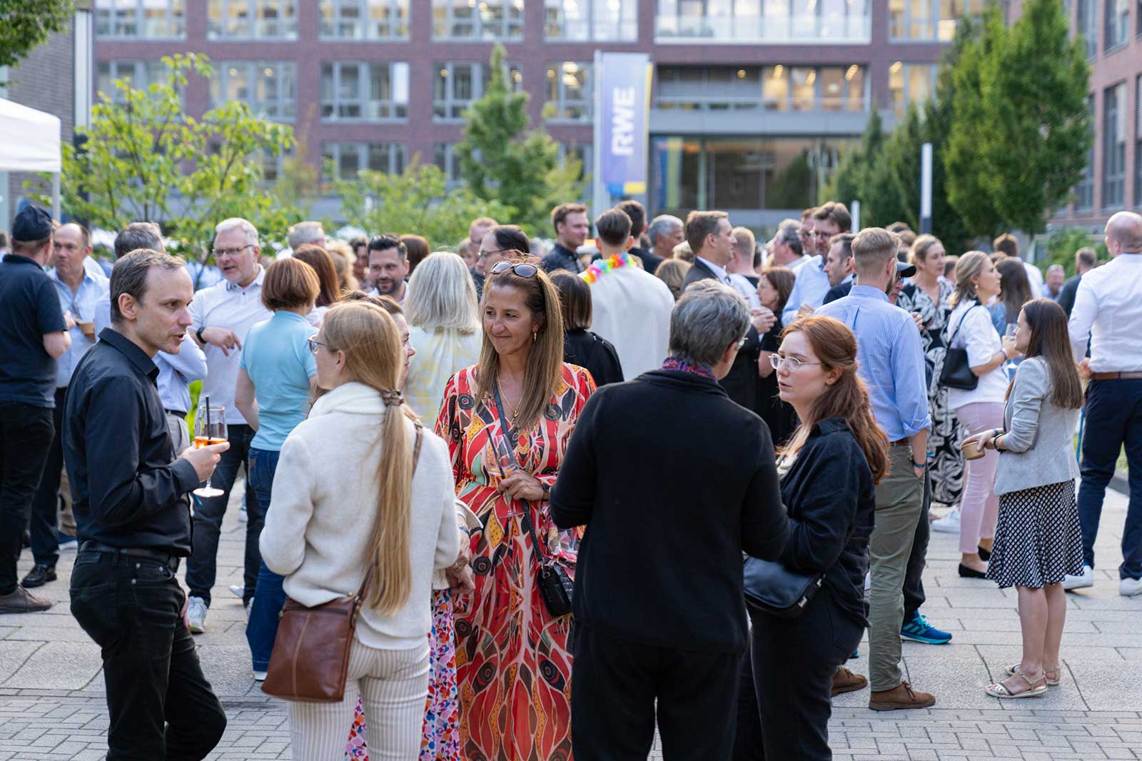 An outdoor gathering with several people holding drinks and engaging in conversation.