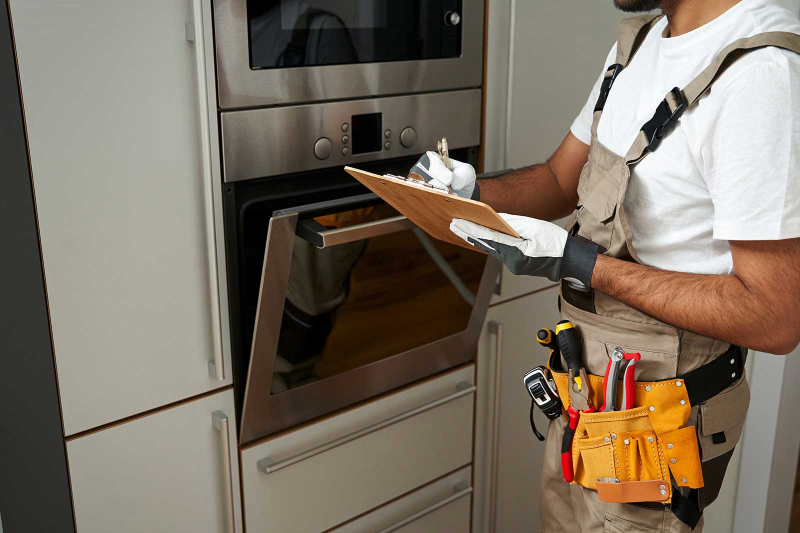 Ein Techniker in Arbeitskleidung prüft einen Ofen, während er Notizen auf einer Holztafel macht.
