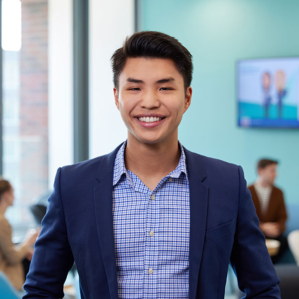A man in a blazer, with short dark hair, stands confidently against a modern office backdrop.