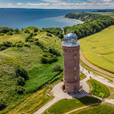 Eine malerische Küstenansicht mit einem Backsteinkliffturm, umgeben von üppigem Grün und einem ruhigen Meer unter einem strahlend blauen Himmel.