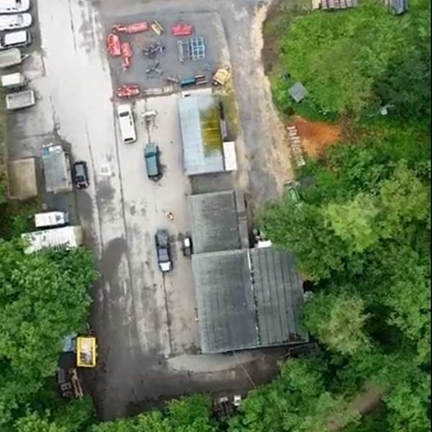 Eine Luftaufnahme eines Lagerbereichs, umgeben von Grün, mit mehreren Fahrzeugen und Industrieausrüstung.