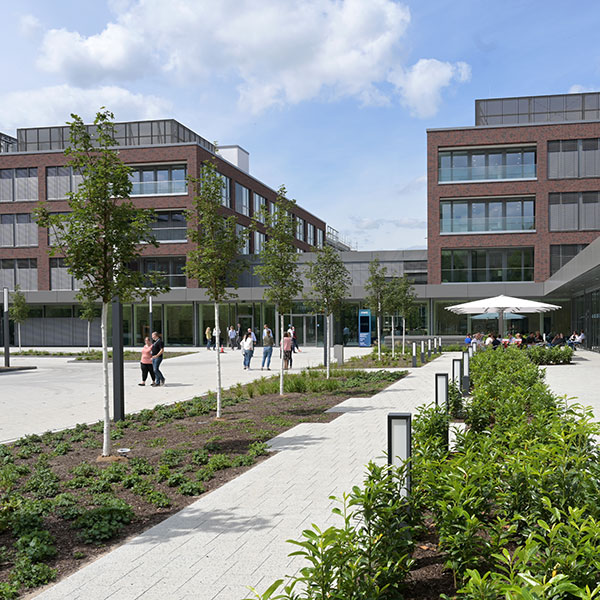 Ein modernes Gebäude mit großen Fenstern, umgeben von Grünflächen und Menschen, die den Außenbereich genießen.
