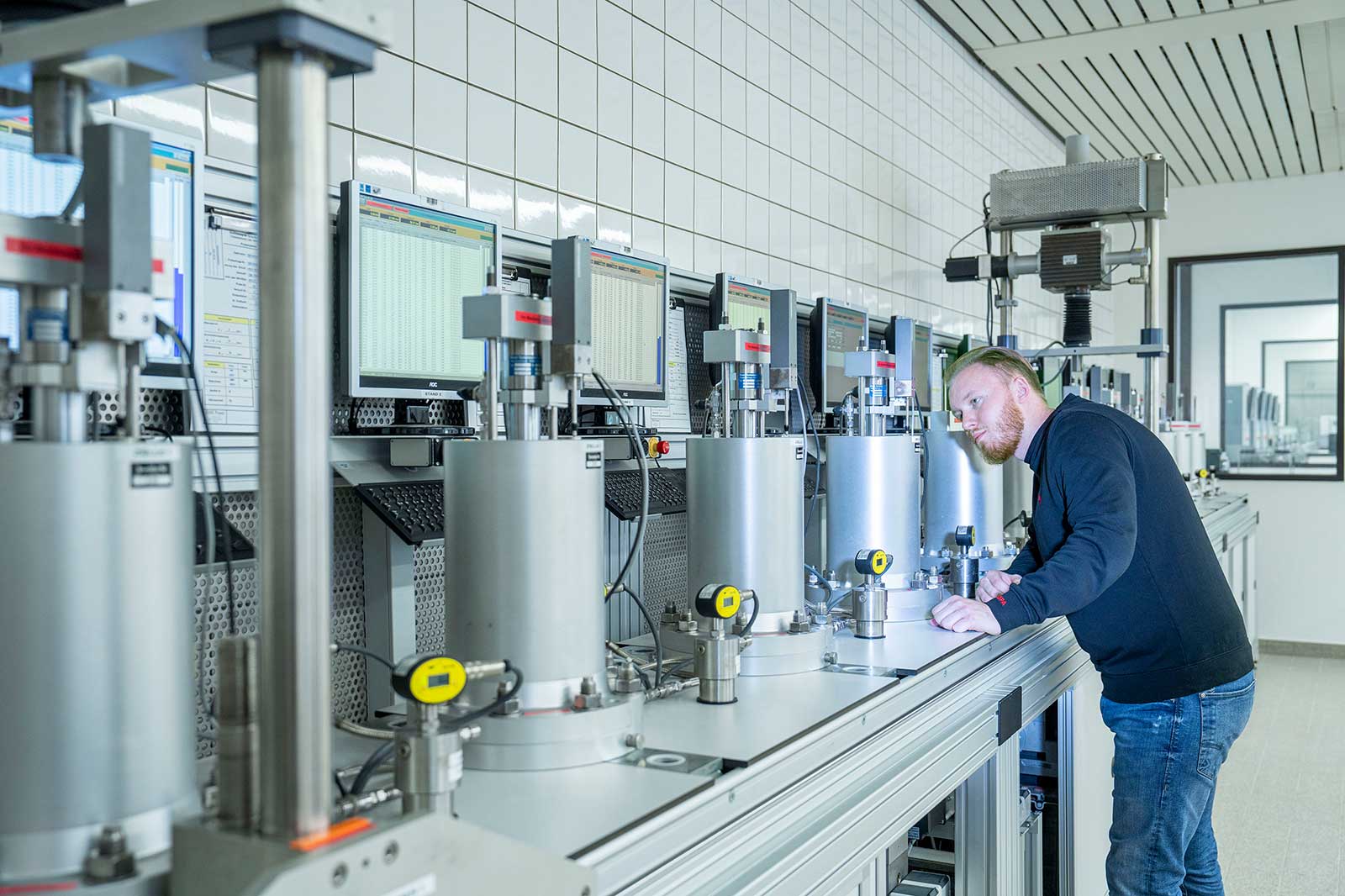 Ein Techniker arbeitet an Maschinen in einem Labor, das mit Monitoren und Präzisionsinstrumenten ausgestattet ist.