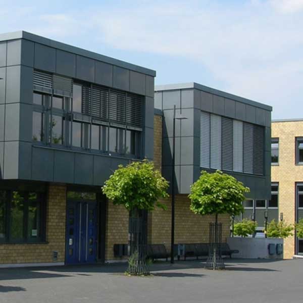 Moderne Architektur mit zwei grauen Gebäuden und großen Fenstern sowie Bäumen davor, vor einem klaren blauen Himmel.