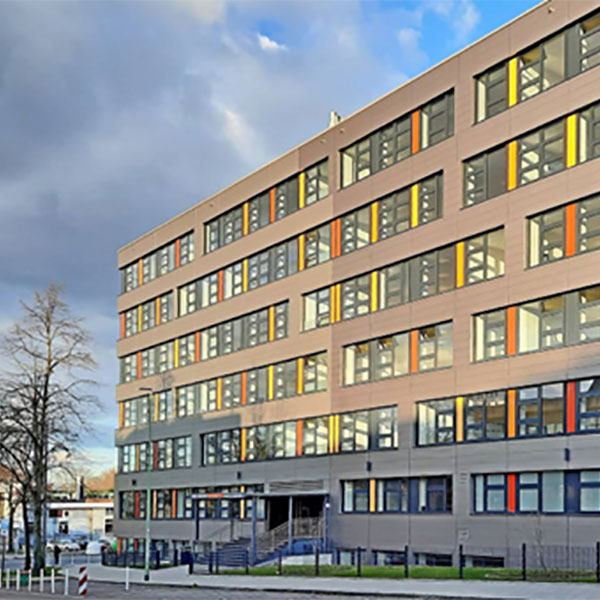 Ein modernes, mehrstöckiges Gebäude mit großen Fenstern und farbenfrohen Akzenten vor einem bewölkten Himmel.