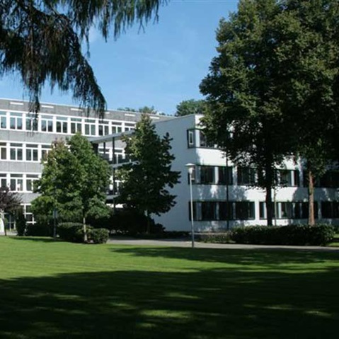 Ein modernes zweigeschossiges Gebäude, umgeben von grünem Gras und Bäumen unter einem klaren blauen Himmel.