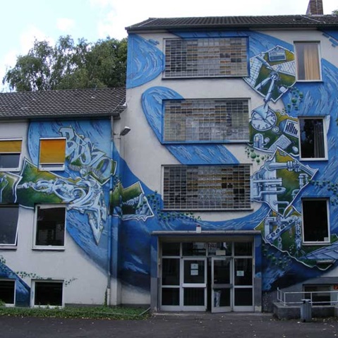 Ein Gebäude mit einem großen Wandgemälde, das blaue Wellen und abstrakte Designs zeigt, die künstlerischen Ausdruck auf seiner Fassade betonen.