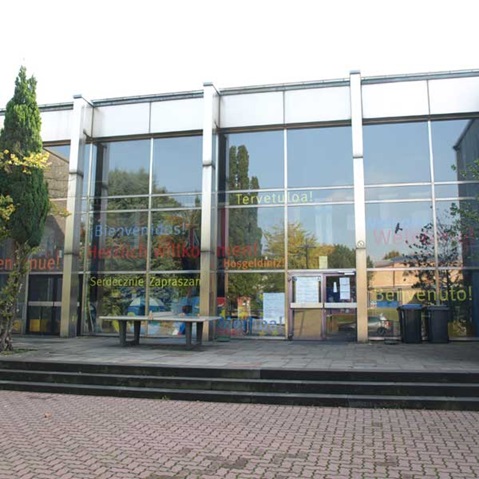 Ein moderner Eingang eines Gebäudes mit Glasfassade und bunten Begrüßungsschildern in mehreren Sprachen.