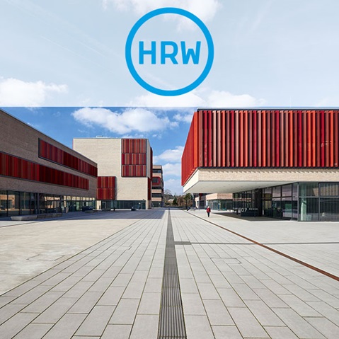 Eine moderne architektonische Landschaft mit roten und beigen Gebäuden auf einem gepflasterten Platz unter einem blauen Himmel mit vereinzelten Wolken.