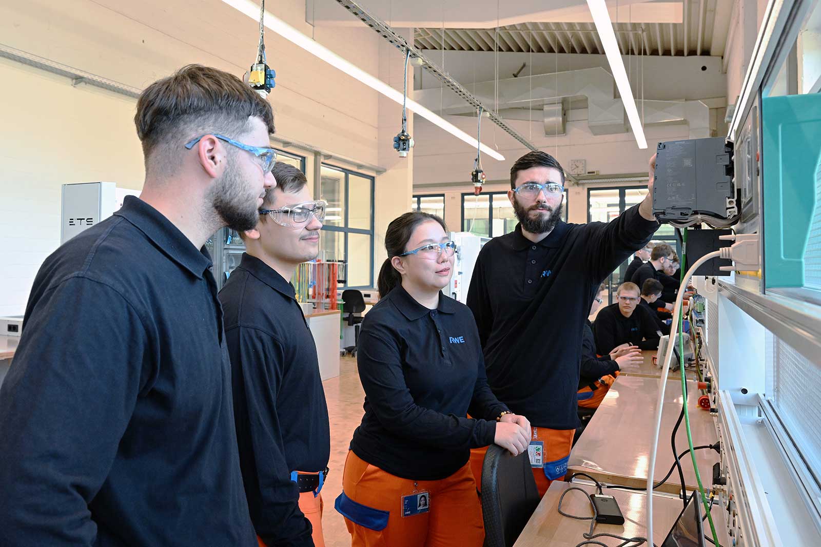 Eine Gruppe von vier Schülern in einem modernen Klassenzimmer, die mit elektronischen Geräten auf einem Tisch arbeiten.