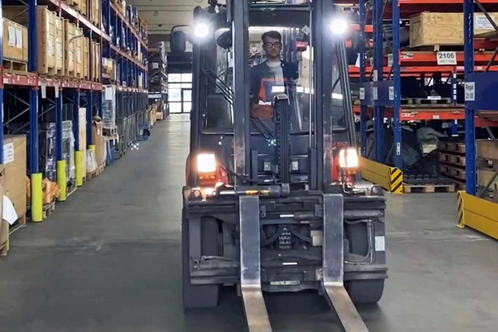 Ein Gabelstapler fährt durch einen Gang in einem Lagerhaus, umgeben von Regalen mit Produkten und Kisten.
