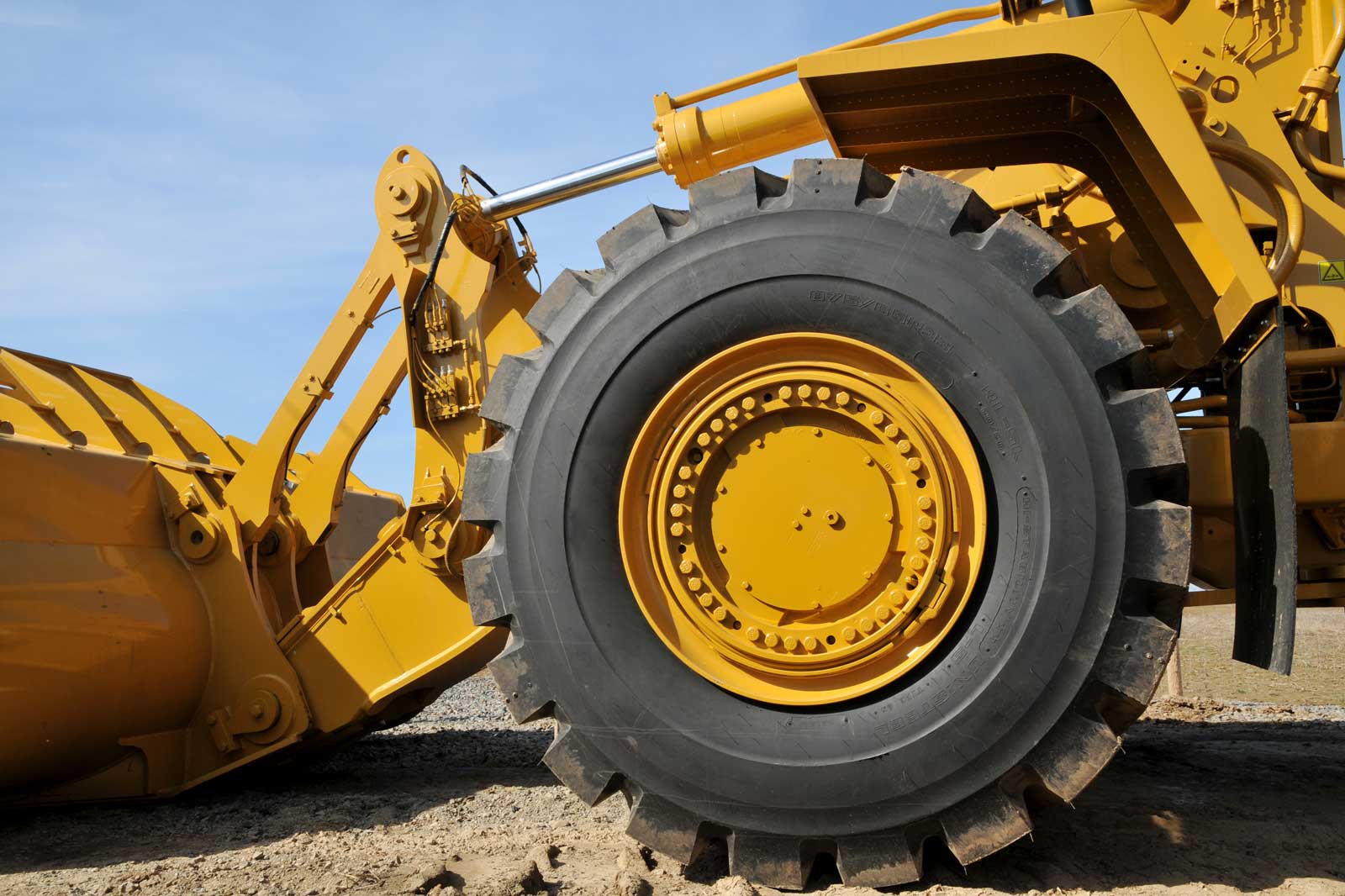 Eine Nahaufnahme des Rades und der Schaufel eines großen gelben Baumaschinenfahrzeugs vor einem klaren blauen Himmel.
