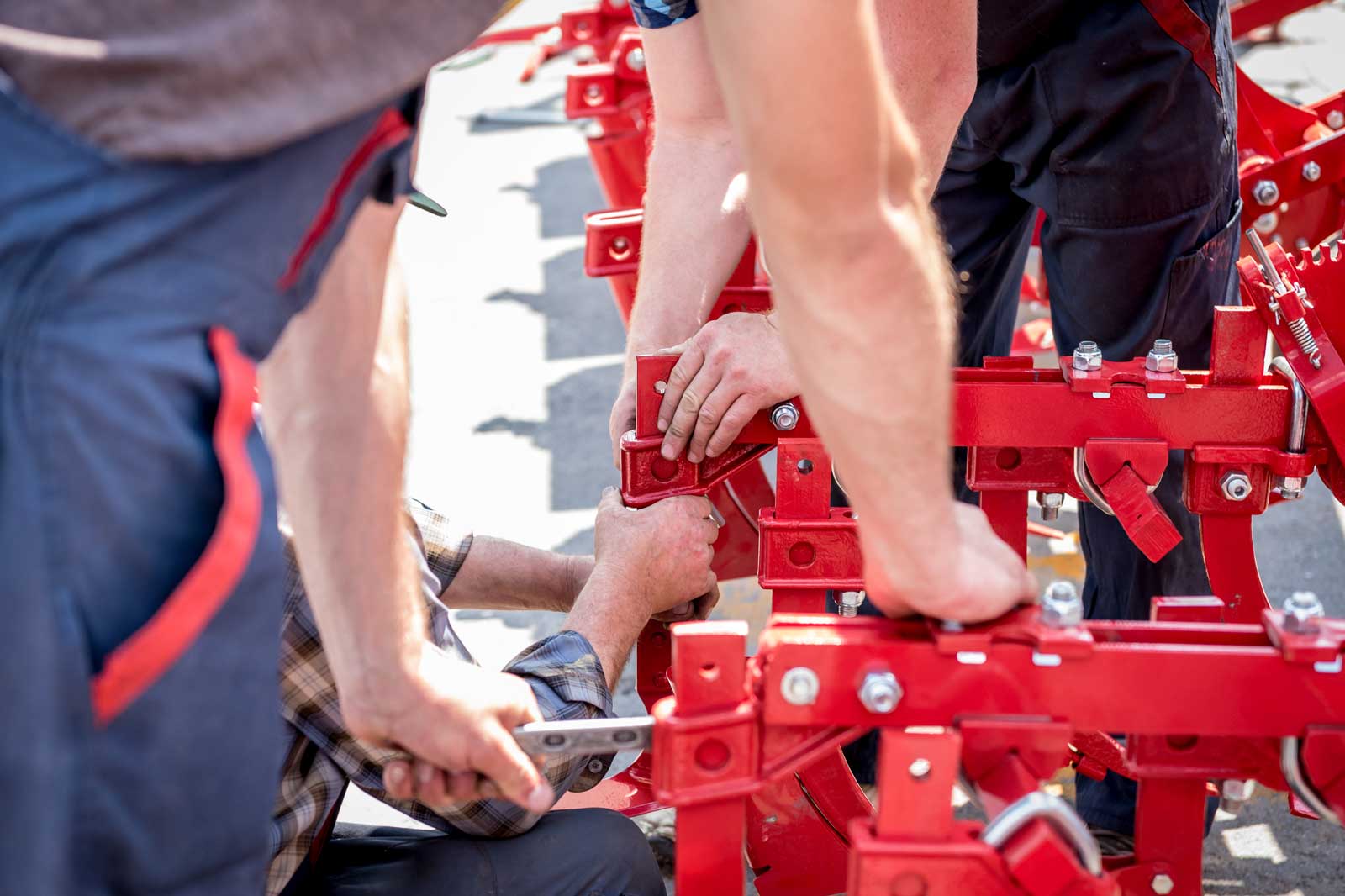 Einige Personen arbeiten zusammen, um eine rote landwirtschaftliche Maschine zusammenzubauen, indem sie Werkzeuge verwenden und gemeinsam handeln.