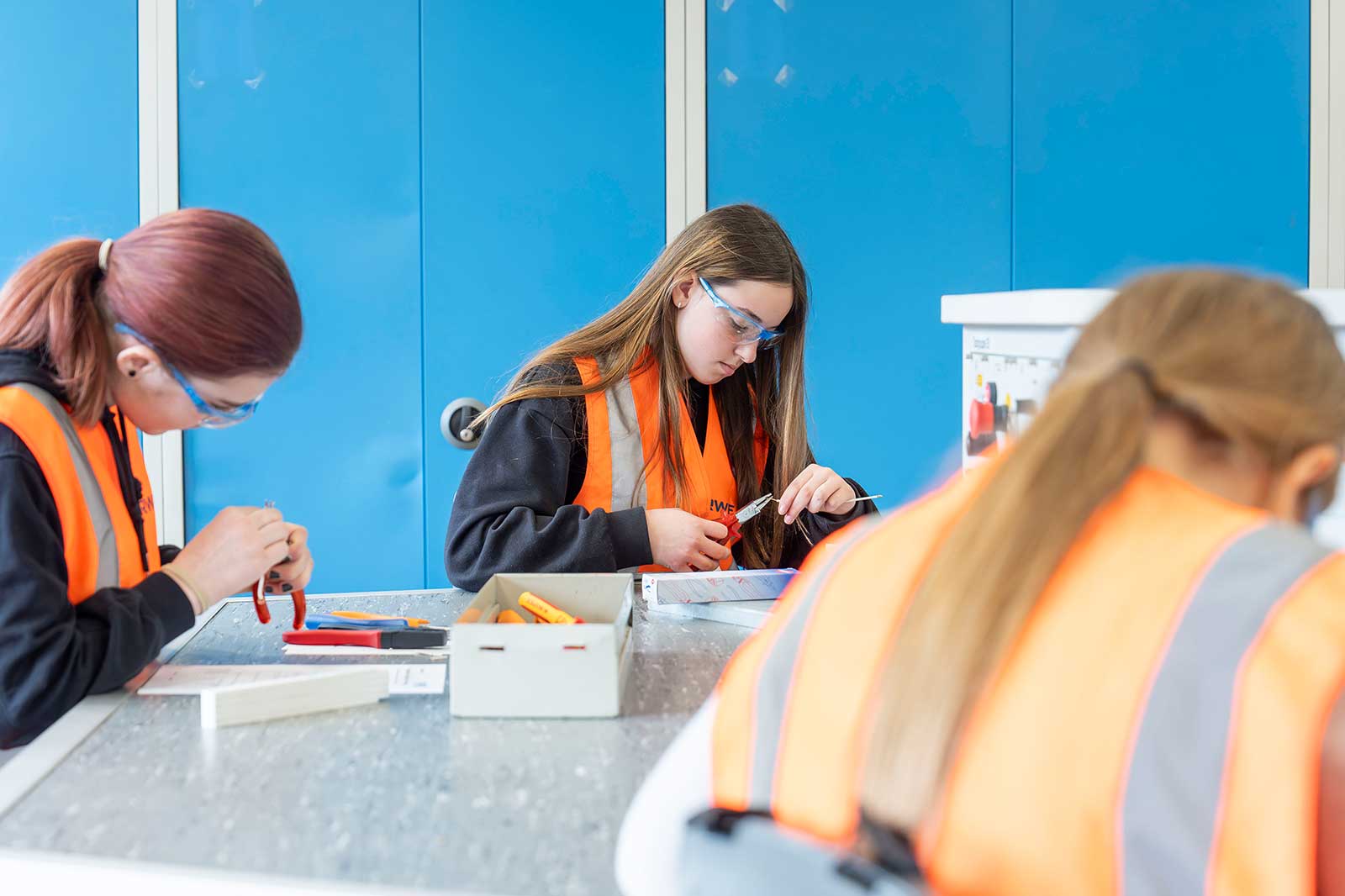 Schüler in Warnwesten arbeiten an einem Projekt an einem Tisch mit verschiedenen Werkzeugen und Materialien.