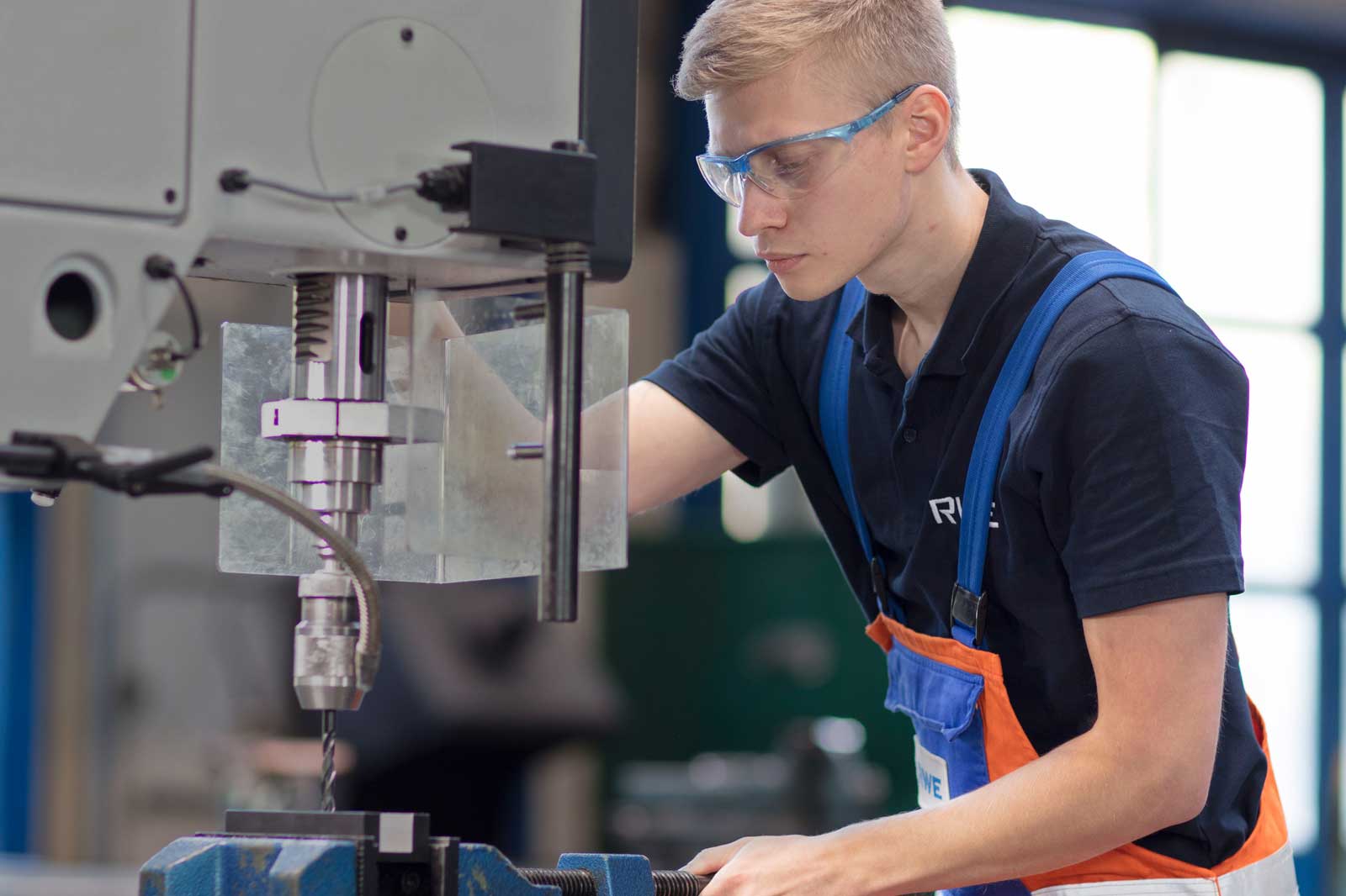 Ein junger Mann arbeitet an einer Bohrmaschine, mit einer präzisen Bohrausrüstung in einer professionellen Werkstatt.