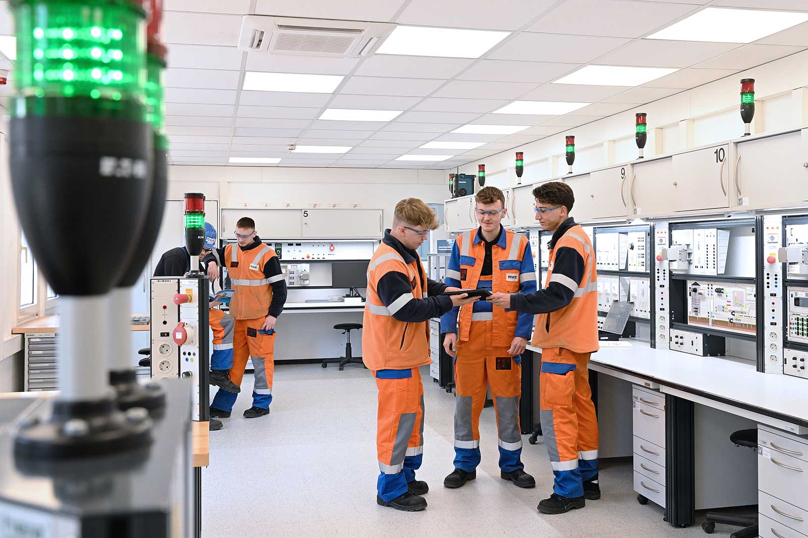 Vier Arbeiter in Sicherheitskleidung diskutieren mit technischem Gerät in einem gut beleuchteten Schulungsraum.