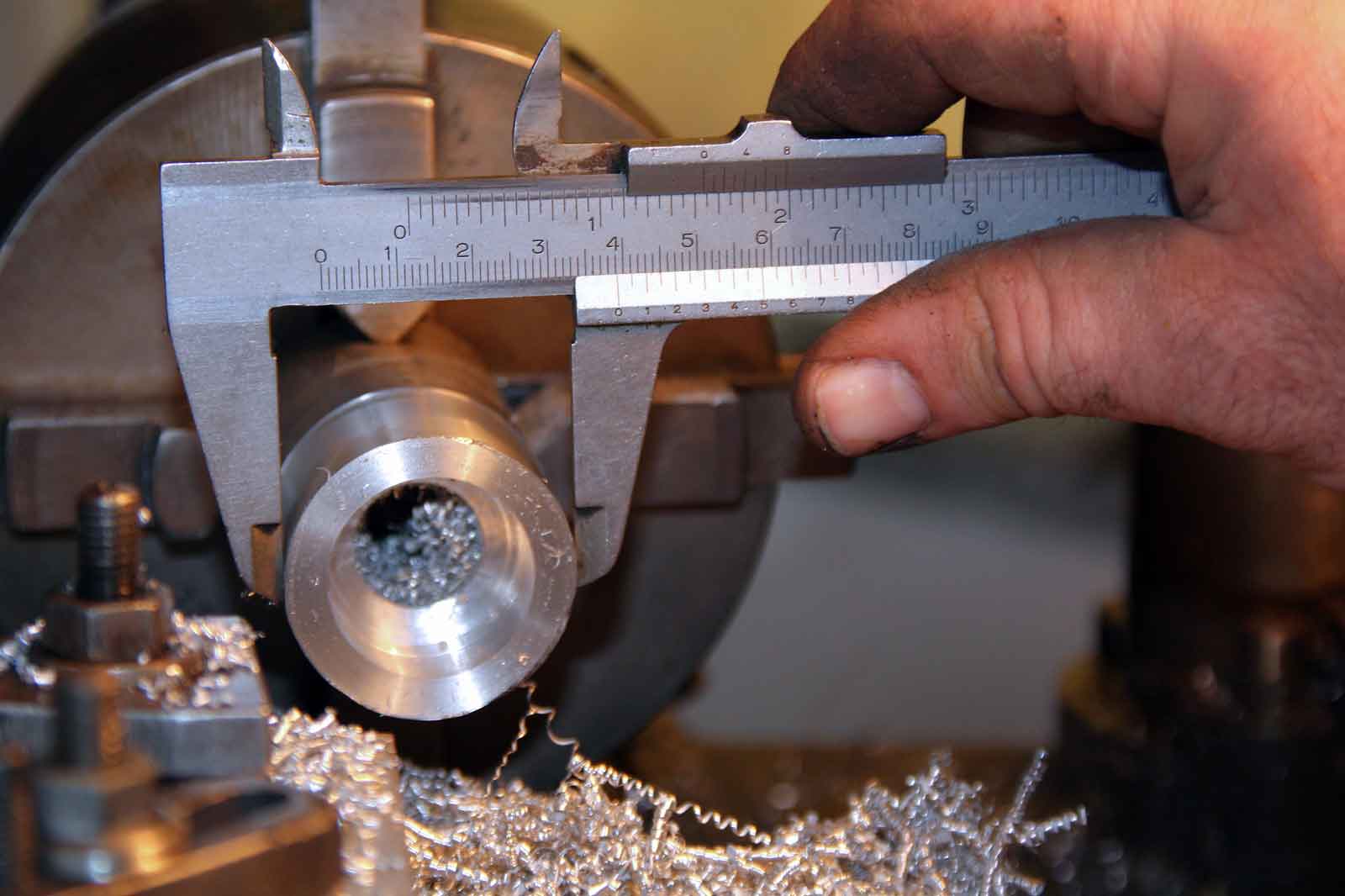 Eine Nahaufnahme einer Hand, die mit einem Messschieber ein glänzendes Metallstück misst, mit Metallspänen auf der Arbeitsfläche.