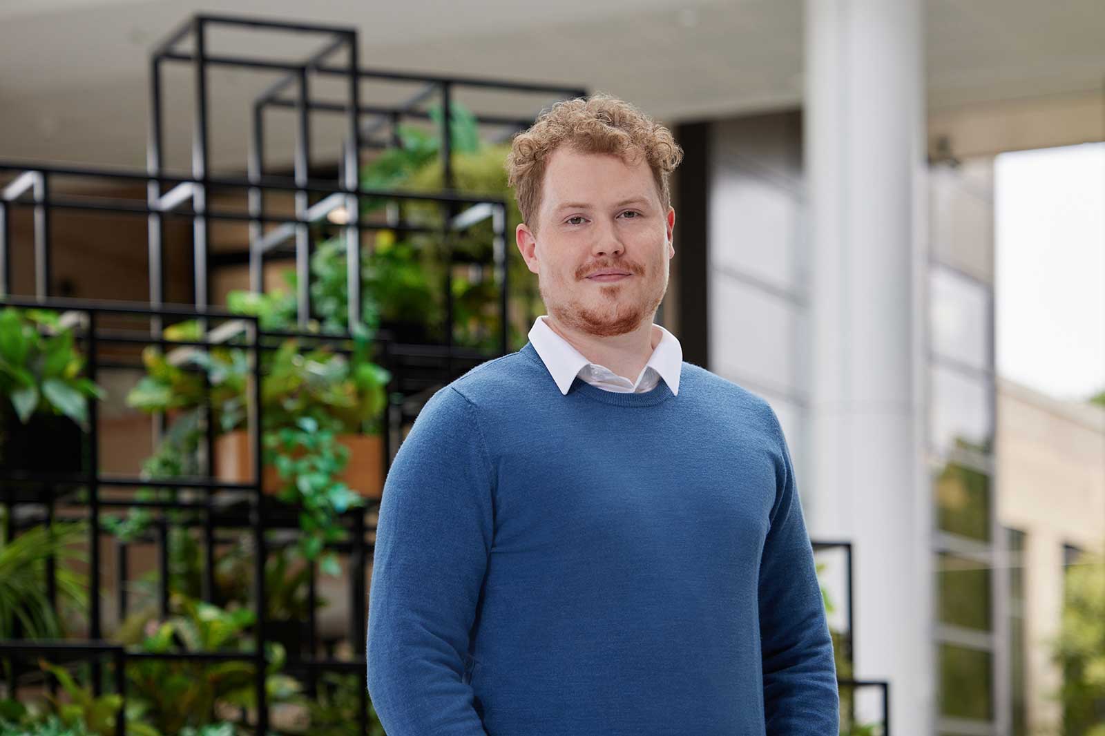 A man stands in front of a modern backdrop featuring plants within an architectural frame.