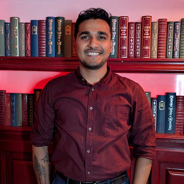 A person stands in front of a shelf filled with old, coloured books, illuminated by red light.
