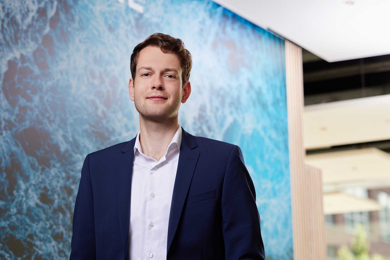 A man in a navy suit stands against a vibrant abstract backdrop of blue and white patterns.
