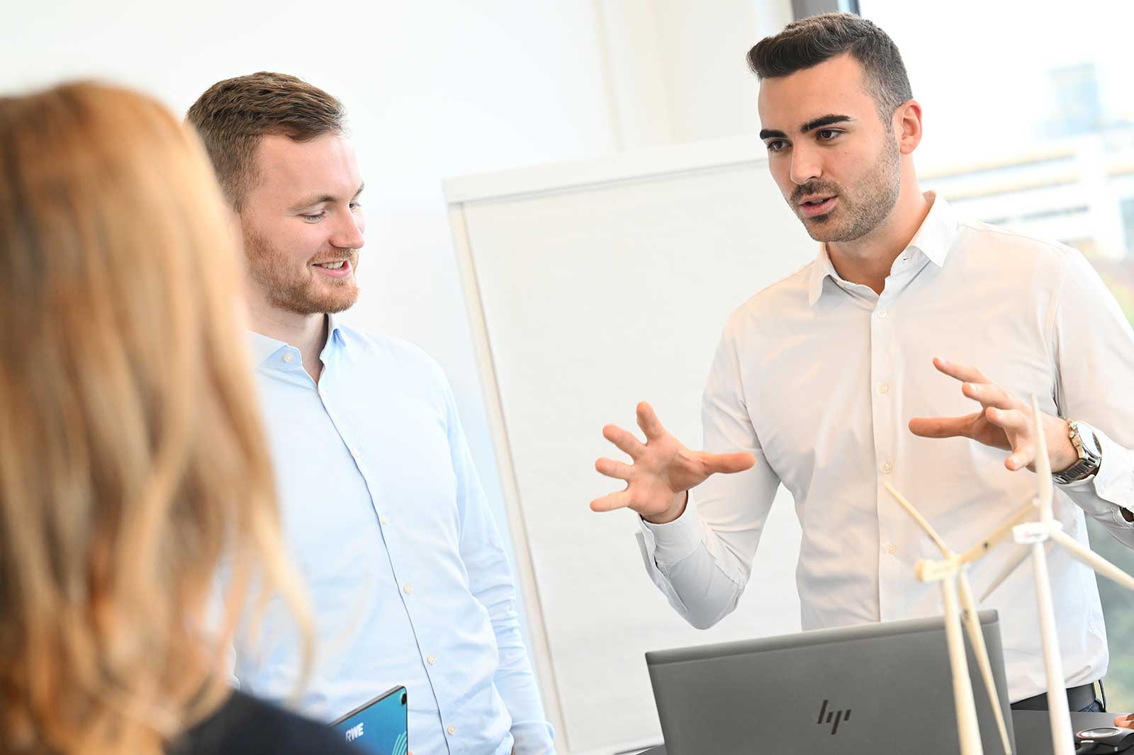 A group of professionals engage in a discussion, with a laptop and small wind turbine models present.