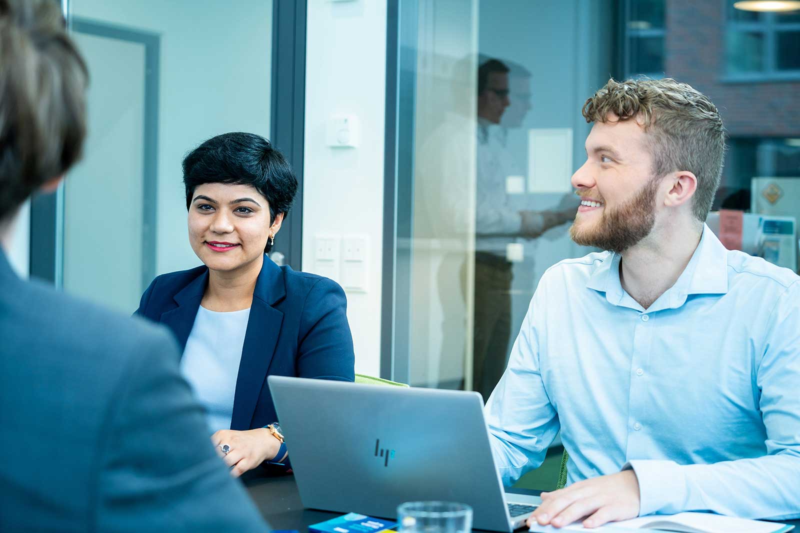 A business meeting with two people at a table, featuring a laptop and some documents visible.