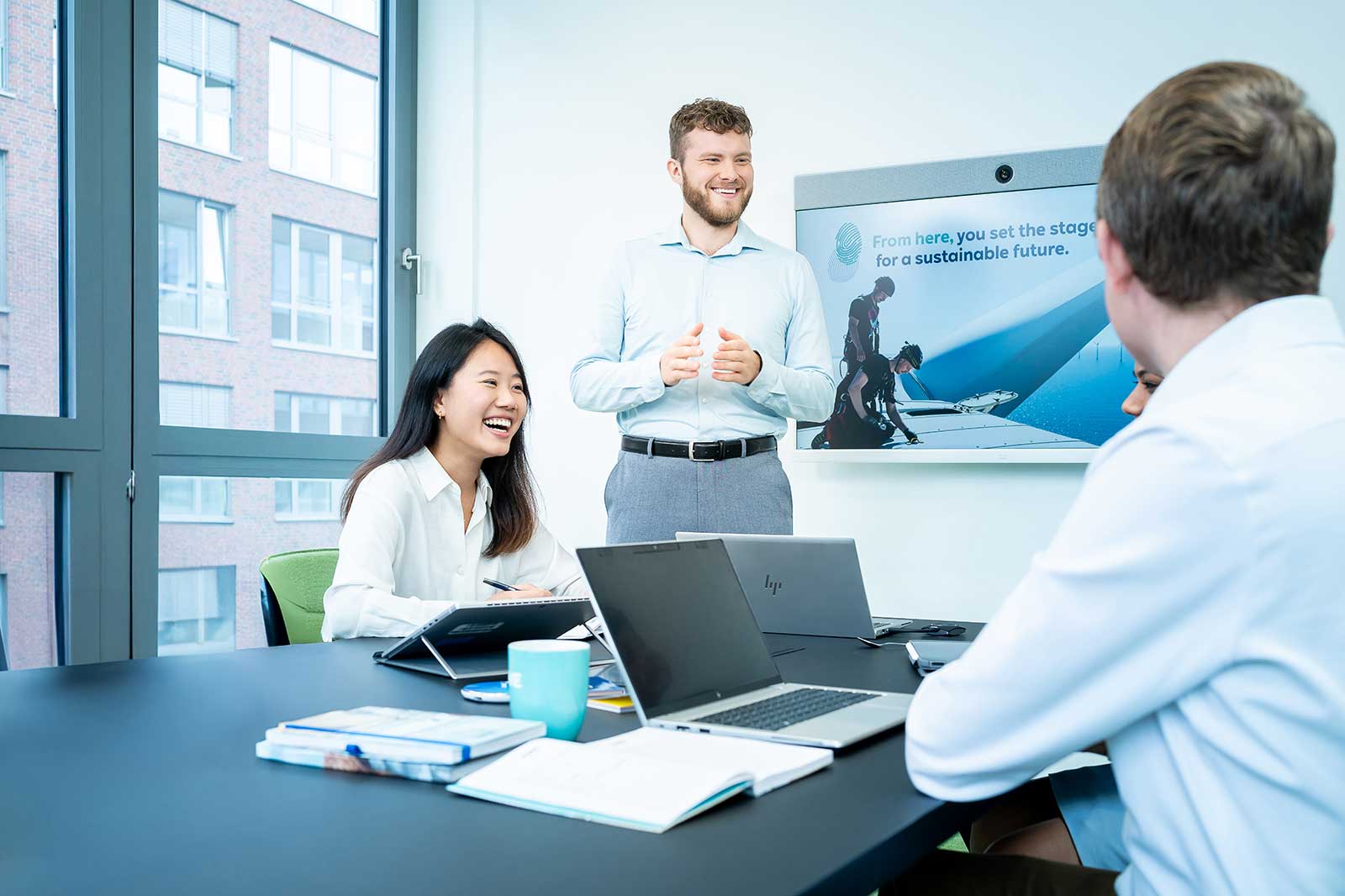 A group meeting in a modern office with a presenter and laptops on the table, focusing on sustainability.