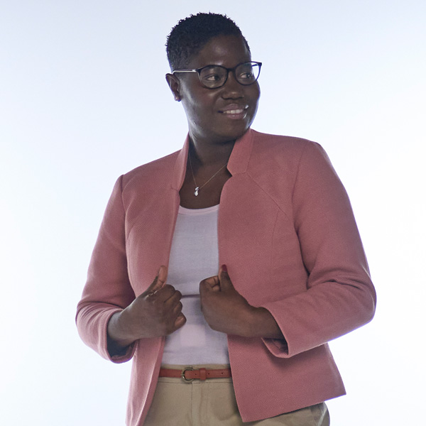 Eine Person trägt ein hellrosa Jackett über einem weissen Oberteil. Sie posiert mit beiden Händen an der Taille.