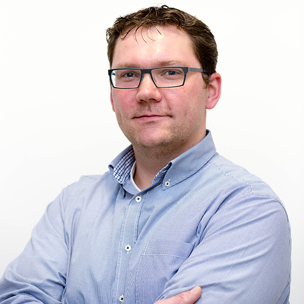 A man with crossed arms is wearing a checked shirt and facing the camera, against a white background.