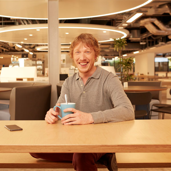 A person sits at a table in a modern café holding a blue cup with a spoon inside.