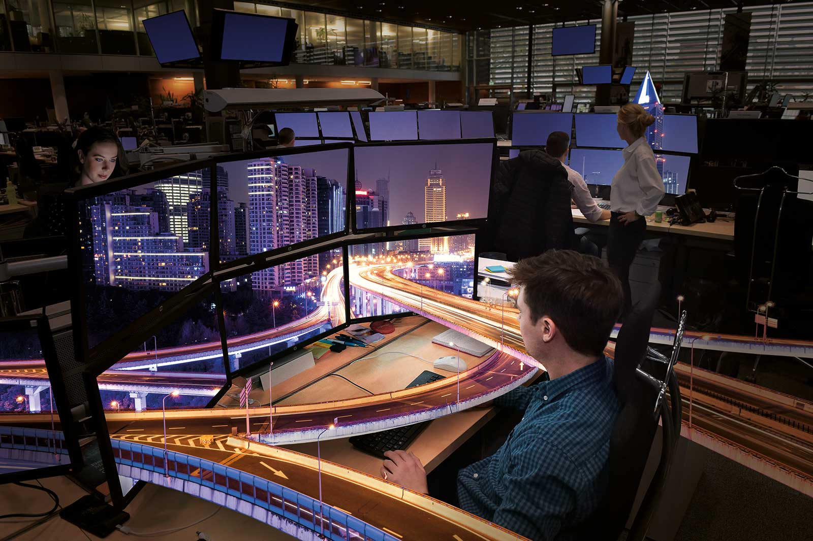 A modern office featuring multiple monitors displaying a city skyline and roadways. A person is seated at a high-tech workstation.