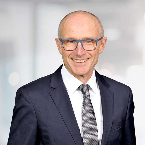 A man in a formal suit and tie stands against a softly blurred background, portrait of Peter Krembel.
