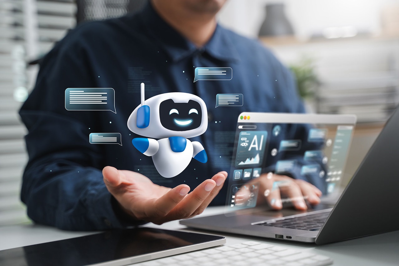 Ein weiß-blauer cartoonartiger Roboter-Hologramm schwebt über einer offenen Hand über einem Schreibtisch mit Laptop und Tastatur, dazu durchscheinende Sprechblasen und ein Bildschirm mit „AI“.