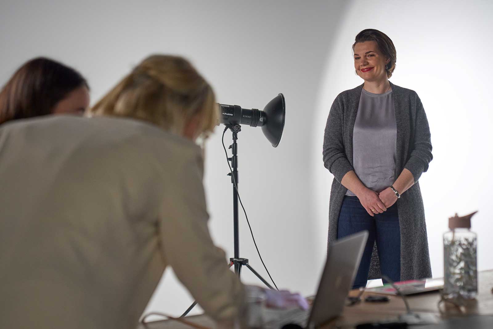 Zwei Personen an einem Tisch, eine steht vor einem Fotostudio-Licht, bereit für ein Fotoshooting.