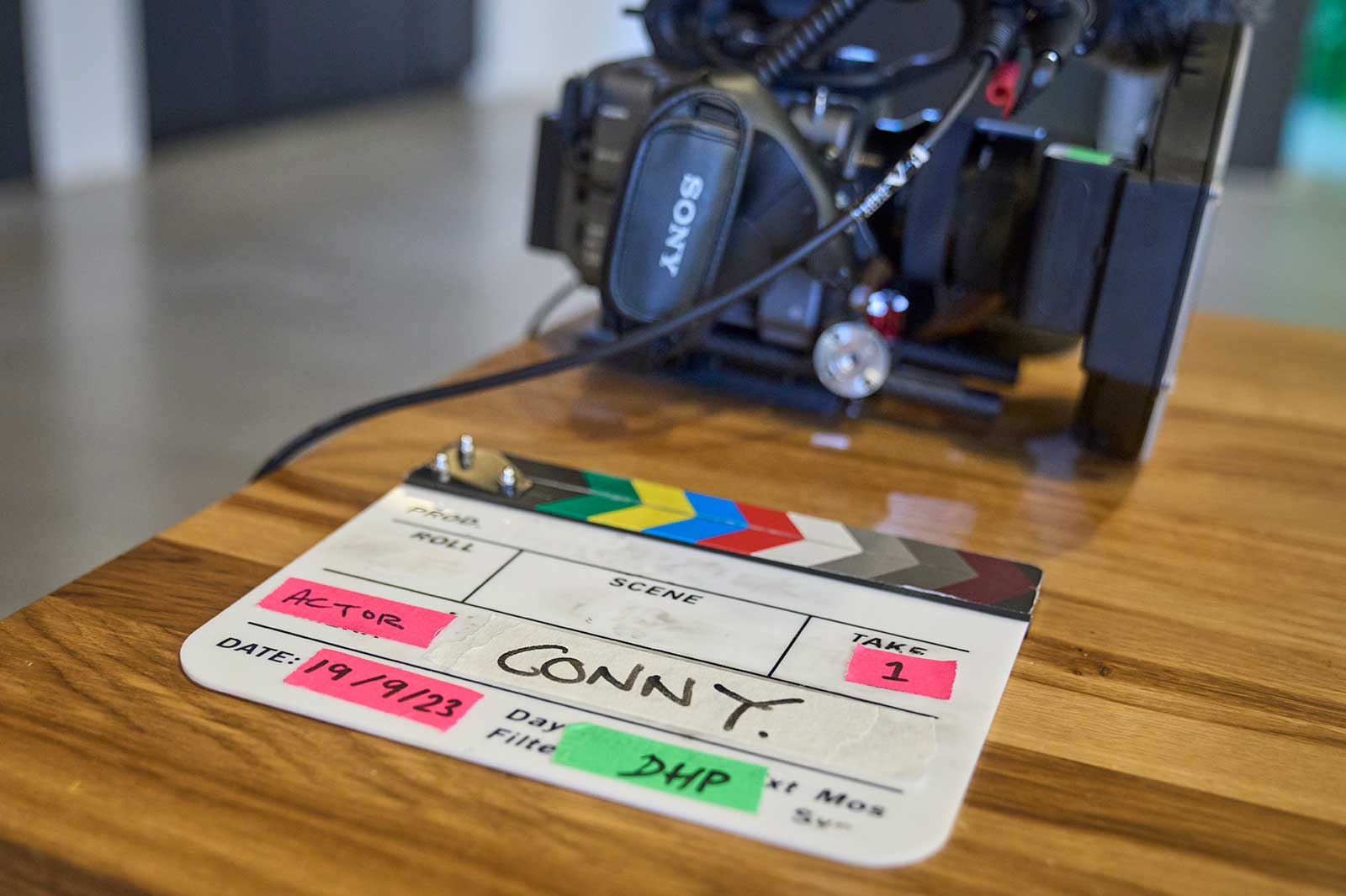 A clapperboard featuring the name 'CONNY', with a camera in the background and the date 19/9/23 on a wooden surface.
