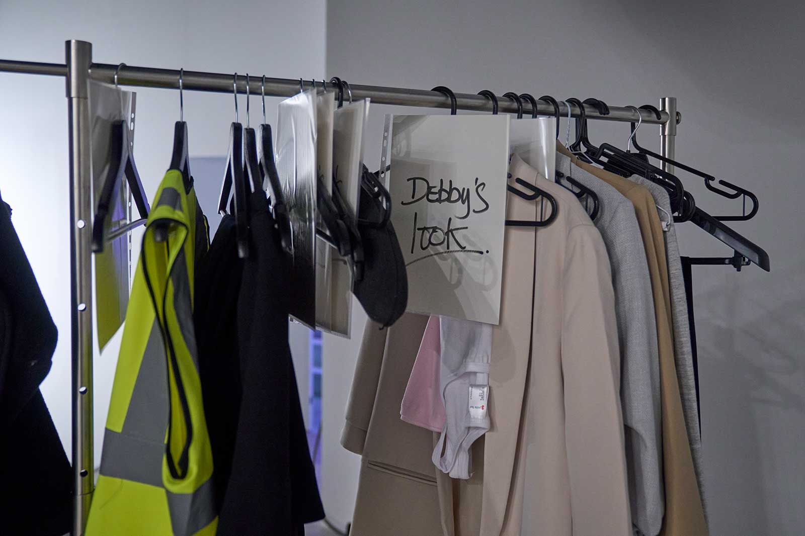 Ein Kleiderständer mit verschiedenen Kleidungsstücken, darunter ein gelbes Sicherheitshemd und eine Notiz mit 'Debby's Look'.