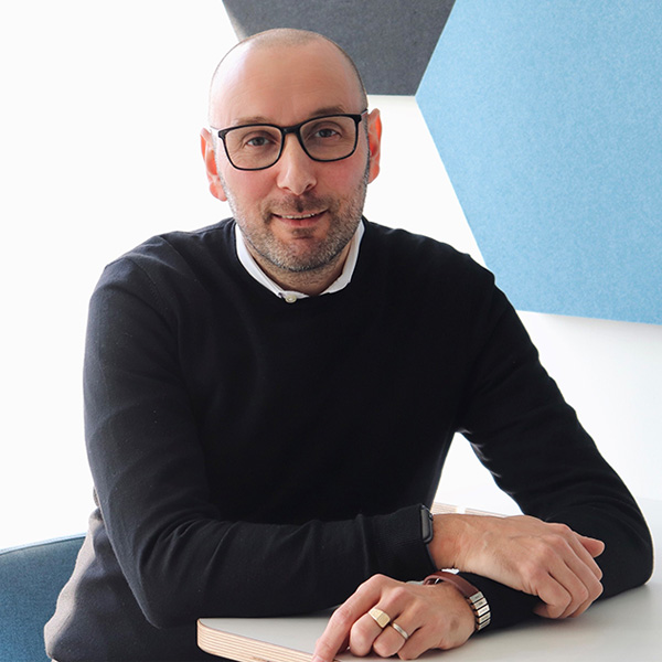 Ein Mann in einem schwarzen Pullover sitzt an einem Tisch, seine Hände liegen auf der Tischplatte. Die Umgebung ist modern gestaltet. Portrait von Joaquin Molina.