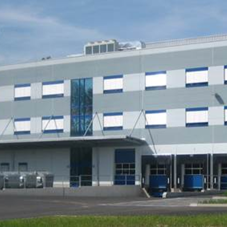 Ein modernes Industriegebäude mit grauen Wänden, blauen Akzenten und großen Fenstern unter einem klaren Himmel.